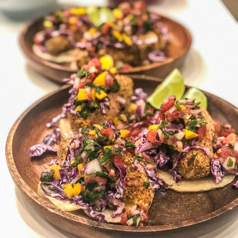 Two wooden plates hold tacos topped with salsa, purple cabbage, and lime. Crispy fillings are seasoned with Gustus Vitae’s World Flavor Favorites Seasonings set of 4, then garnished with tomatoes, peppers, and fresh herbs.