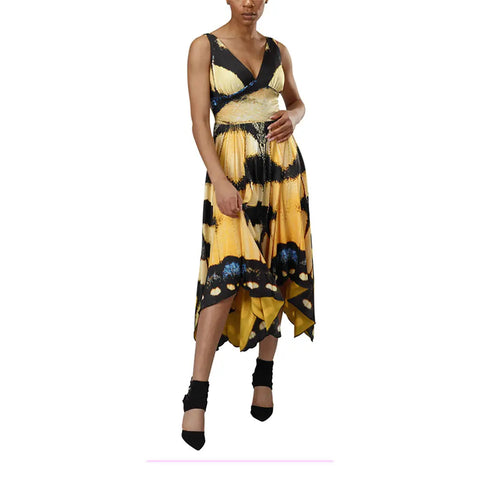 A woman models the Spiritex Yellow Swallowtail Butterfly Dress, a sleeveless V-neck with an asymmetrical hem inspired by its namesake, styled with black ankle-strap heels.