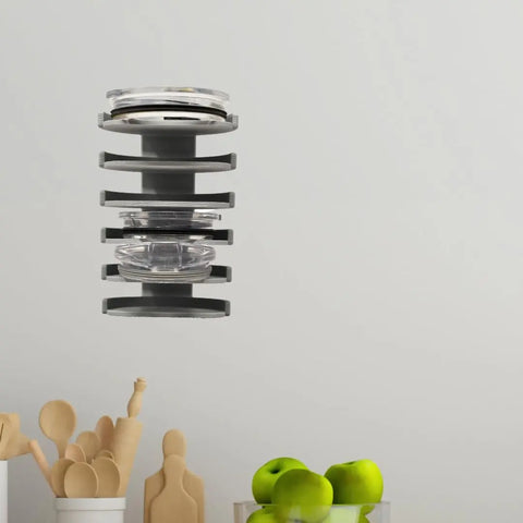 The Yeti Lid Mount Rack by Chatelet Manufacturing is a stackable kitchen organizer for lids and clear food containers, mounted on a light-colored wall above wooden utensils, cutting boards, and a bowl of green apples.