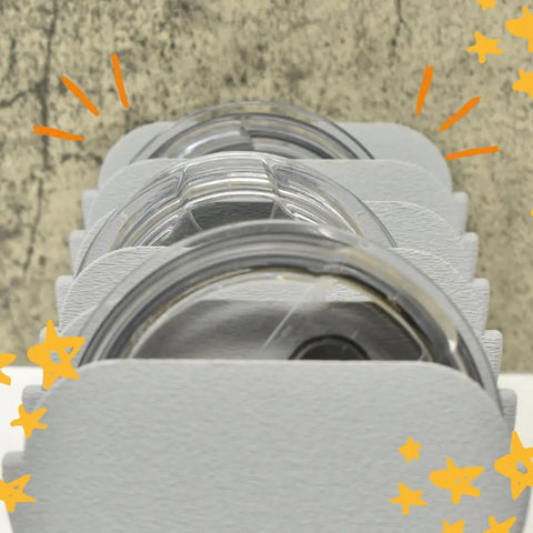 Close-up of stacked clear cup lids with gray dividers in a Chatelet Manufacturing Yeti Lid Mount Rack, decorated with hand-drawn orange stars and lines on the sides.