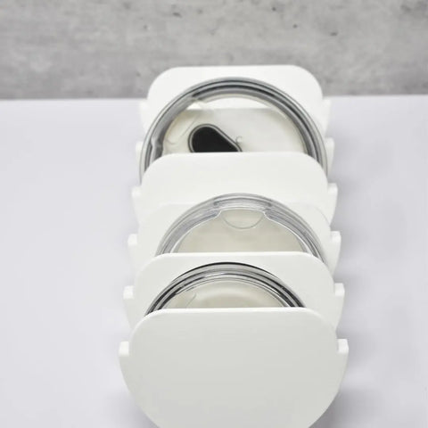 Four Yeti tumbler lids are stored vertically in the Chatelet Manufacturing Yeti Lid Mount Rack, displayed on a light surface. The clear lids have assorted spout styles with black or silver accents, ideal for kitchen lid organization.