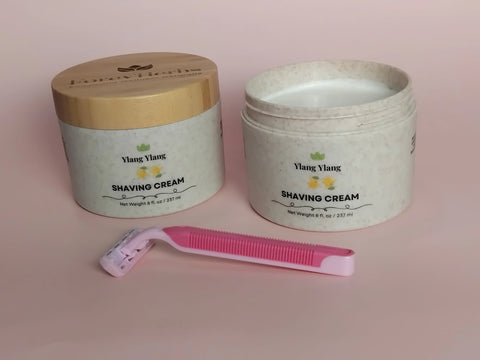 Two Forev’Herbs Ylang Ylang Shaving Cream containers, one open to show the moisturizing formula, with a pink disposable razor on a pale pink background—ideal for preventing razor bumps.