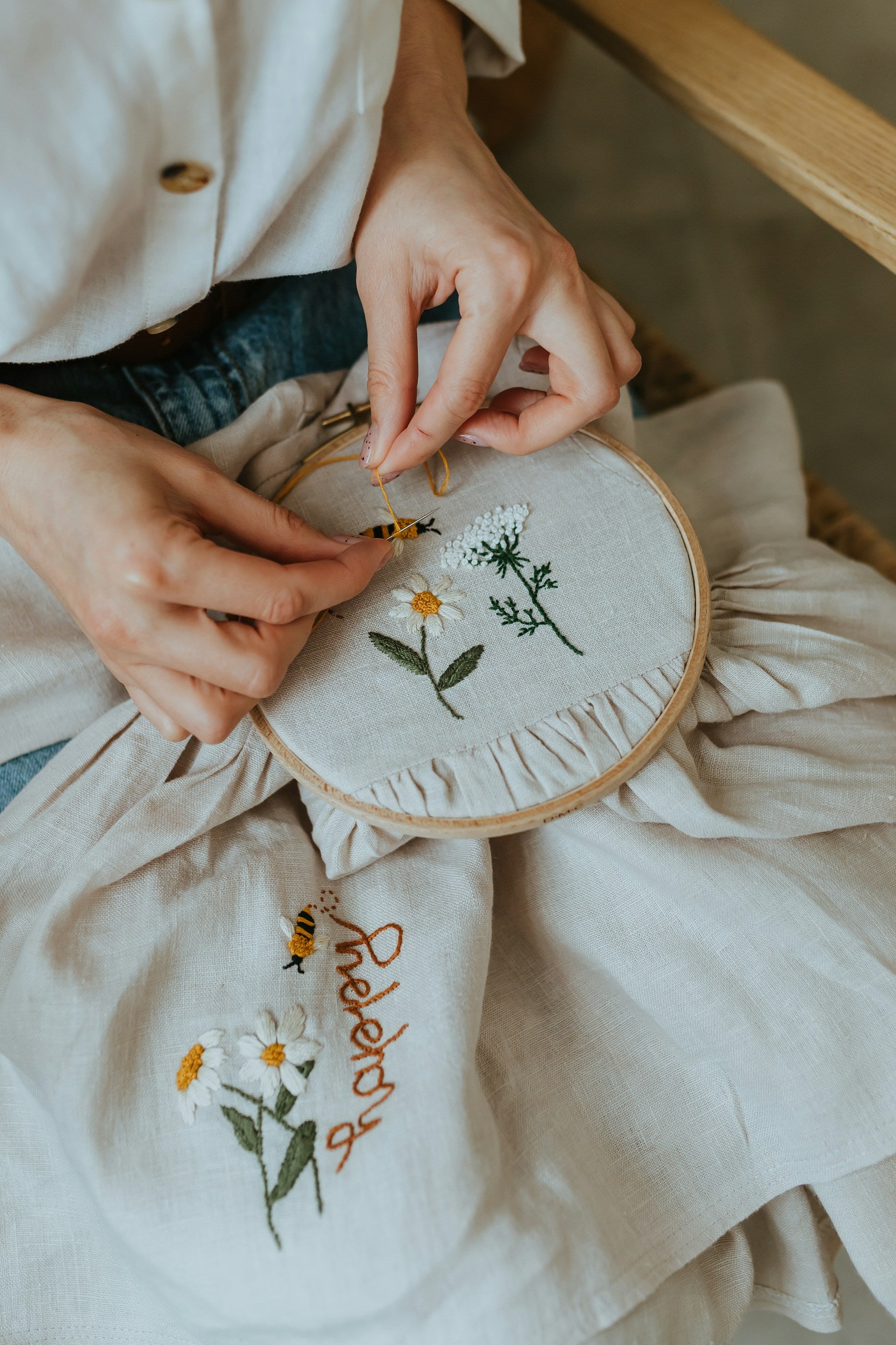 Person embroiderying flowers on a piece of fabric with a wooden hoop.