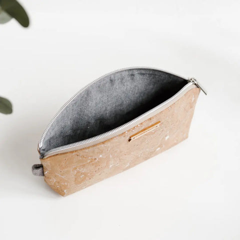 The RULE BREAKER zippered pouch | SILVER by Carry Courage, featuring a tan marbled cork exterior and gray fabric lining, sits open on a white surface with a small green plant partially visible in the corner.